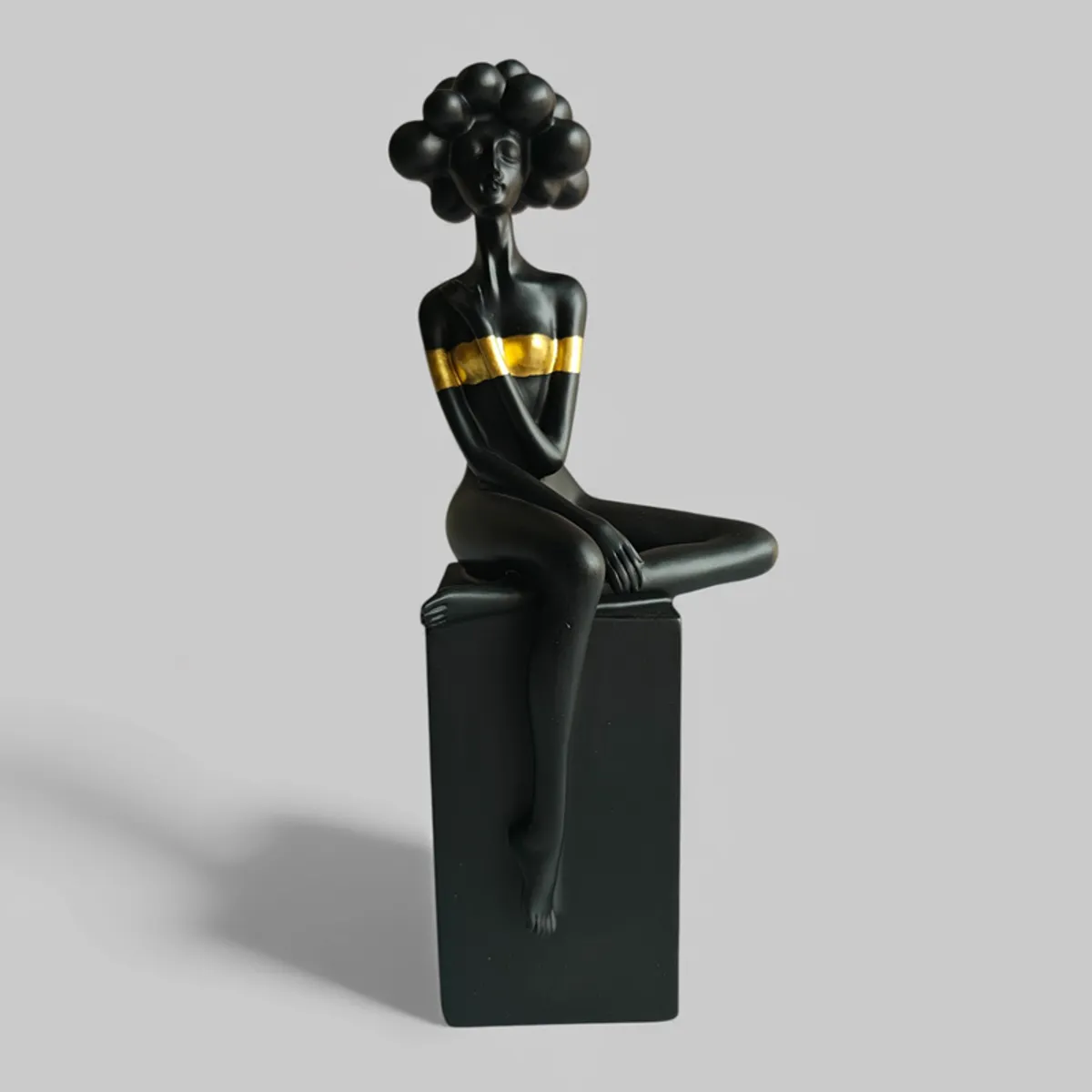 Glossy black and gold sitting lady figurine shown against a plain grey background