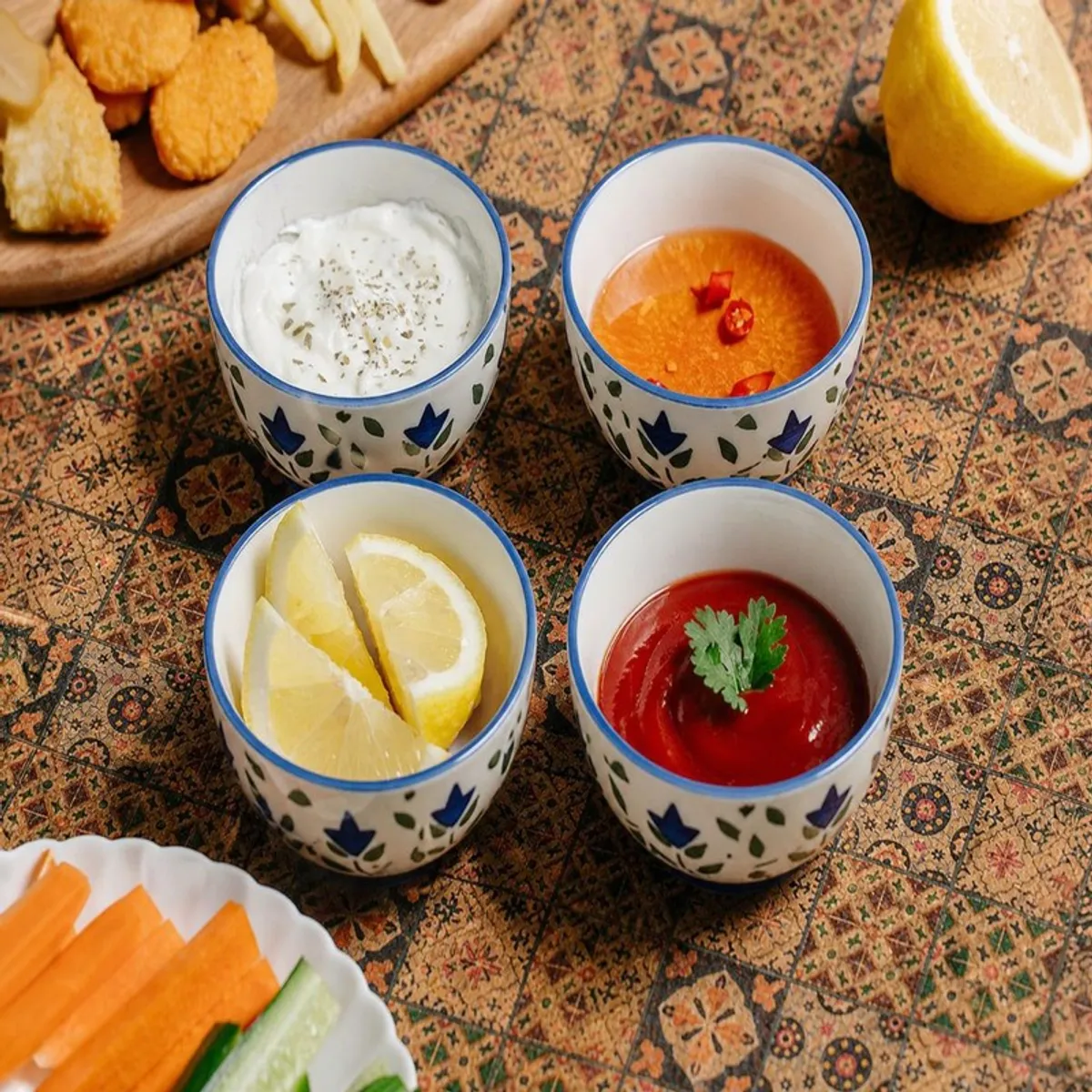 Four blue and white floral snack bowls holding dips, fruit and lemon wedges