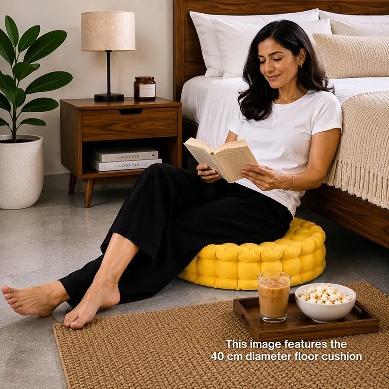 Person seated on a mustard yellow floor cushion beside a bed