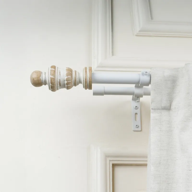 White double curtain rod with antique-style urn finial mounted beside a curtain