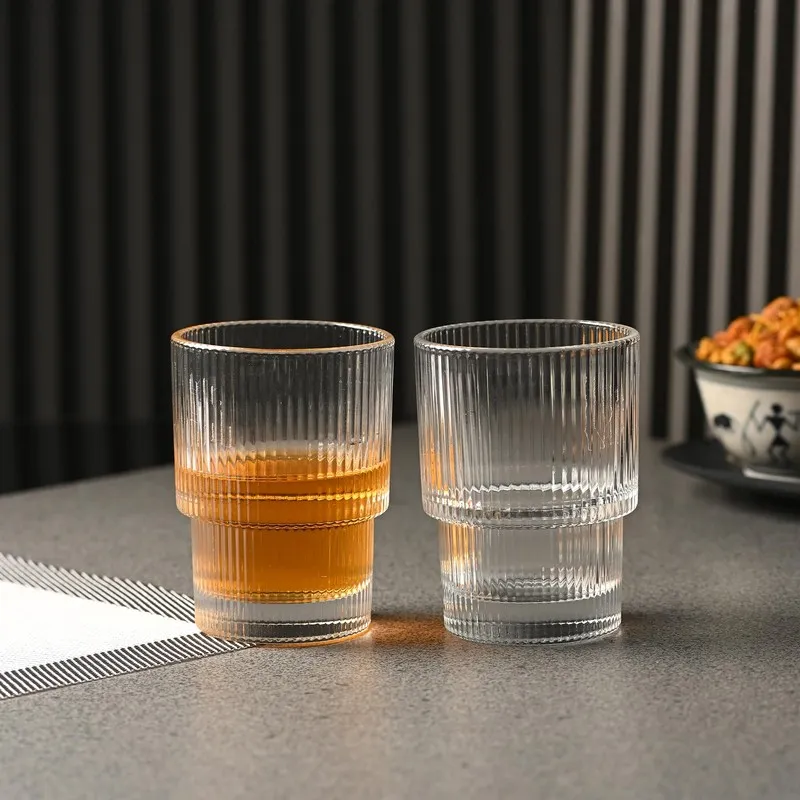 Two clear ribbed cocktail glasses on a tabletop, one filled with amber drink