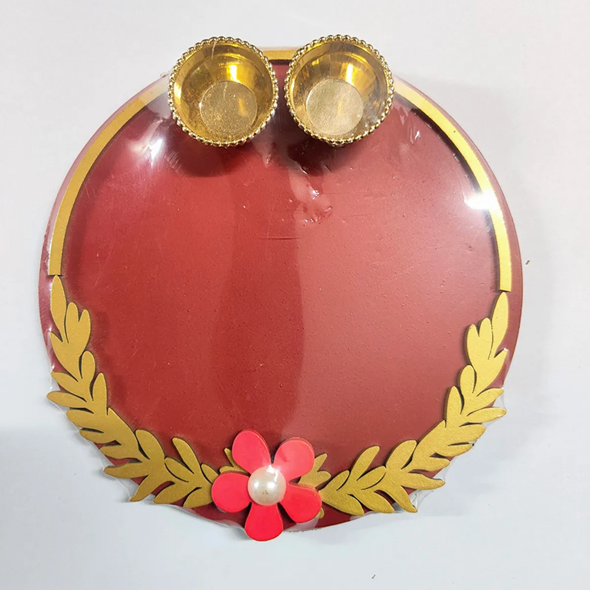Top view of maroon pooja thali with gold leaf border, flower detail and two bowls