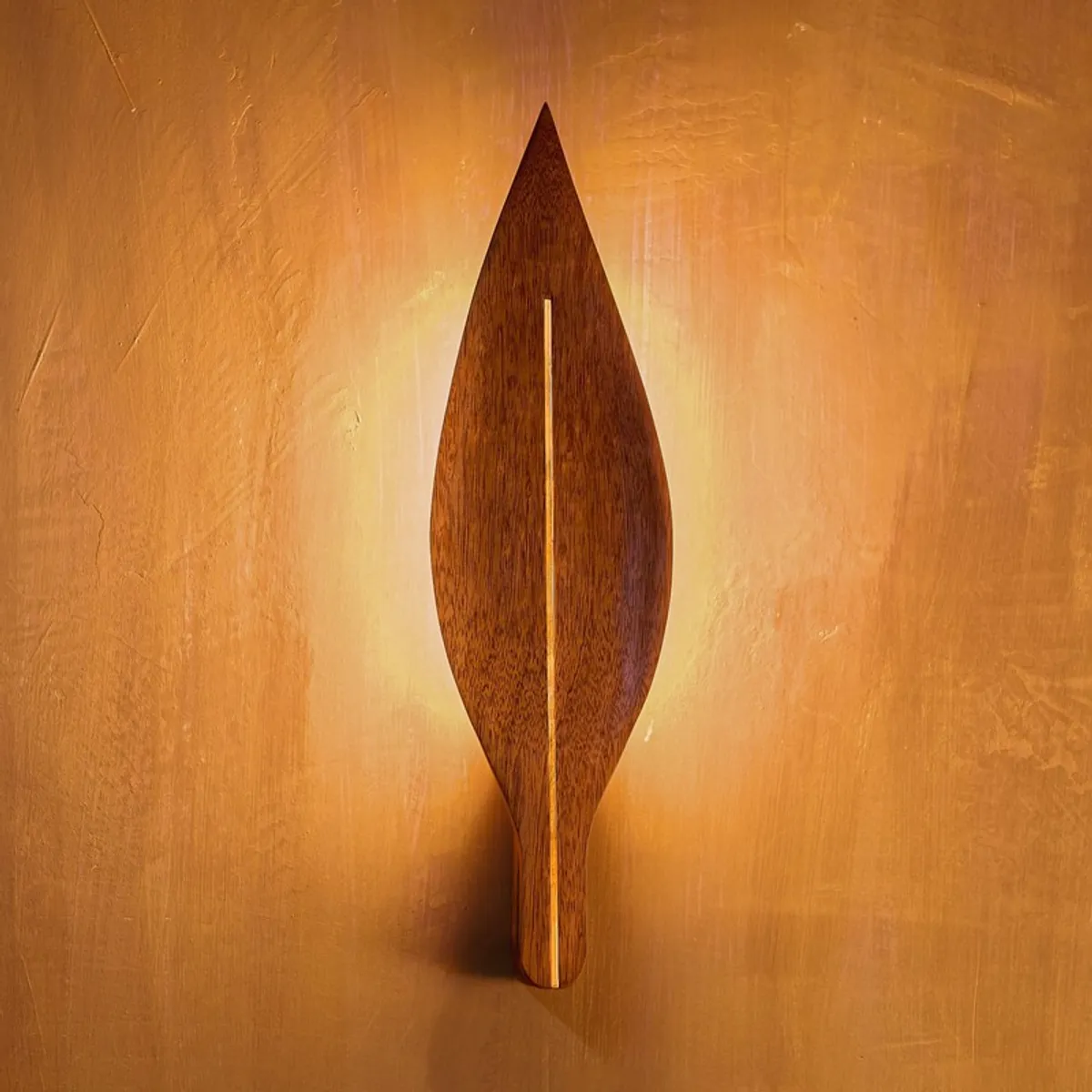 Centered view of a brown leaf wall lamp lit against a warm textured wall