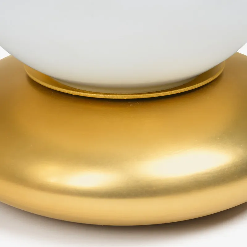 Close-up of the gold base and lower edge of the white glass shade