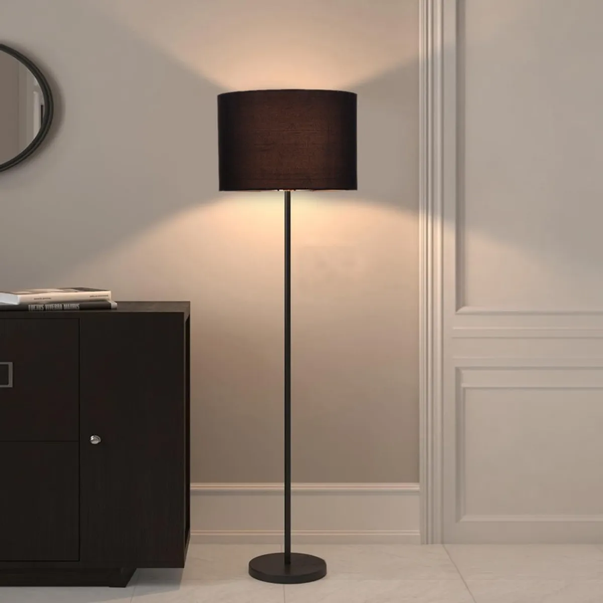 Black drum shade floor lamp glowing beside a dark cabinet