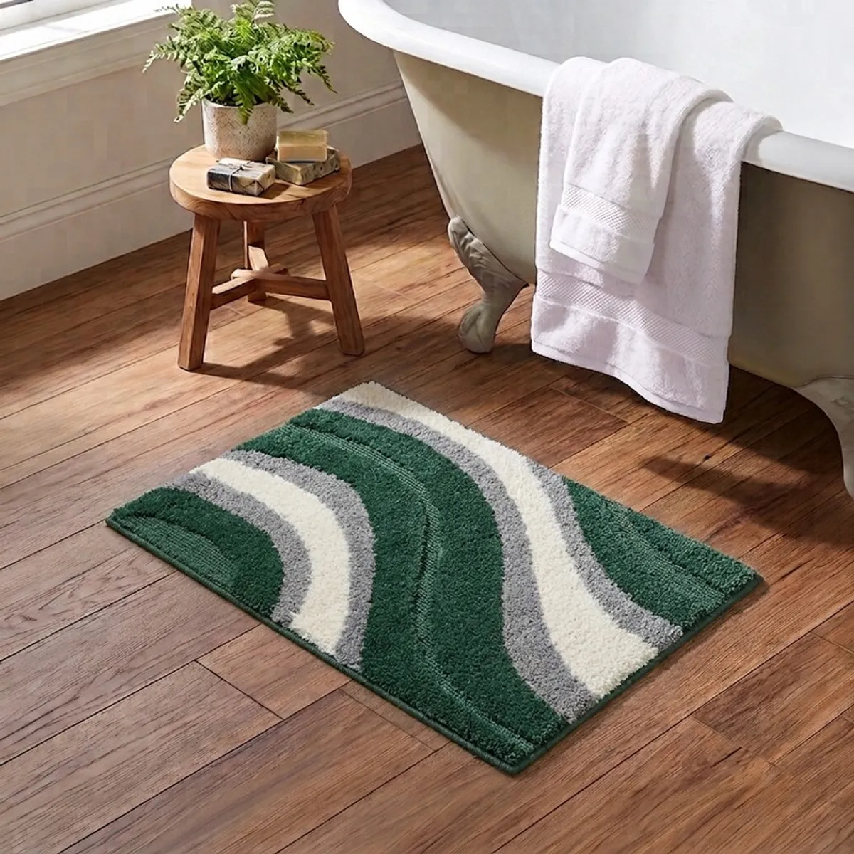 Green rectangular bath mat with curved grey and off-white wave bands on a wooden bathroom floor