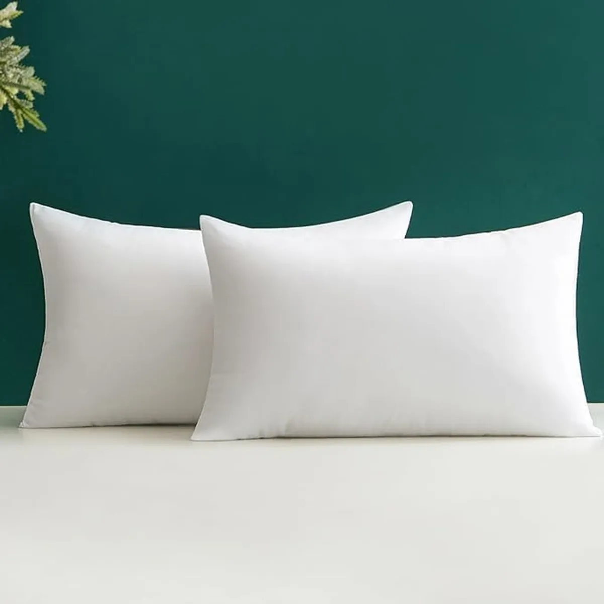 Two white rectangular pillow fillers displayed against a dark green background.