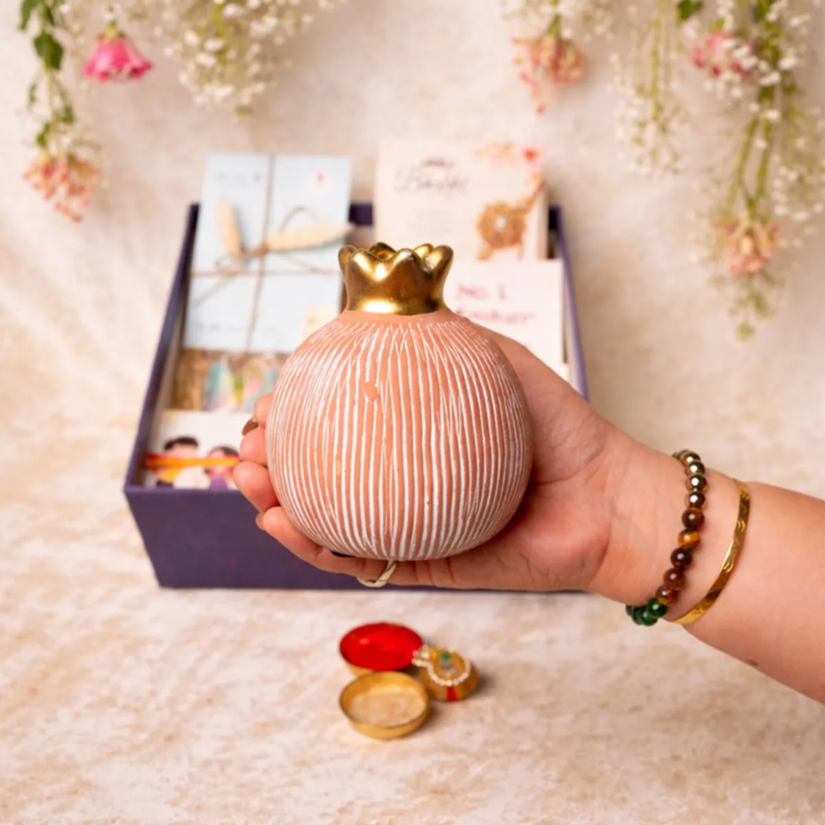 Hand holding the ivory pomegranate ceramic vase above the open blue gift box