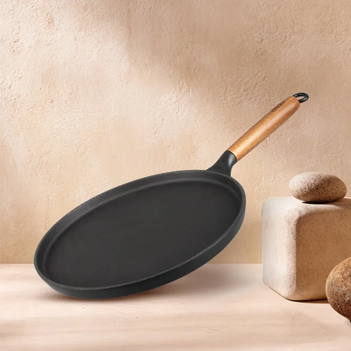 Black round dosa tawa with wooden handle displayed against a neutral backdrop