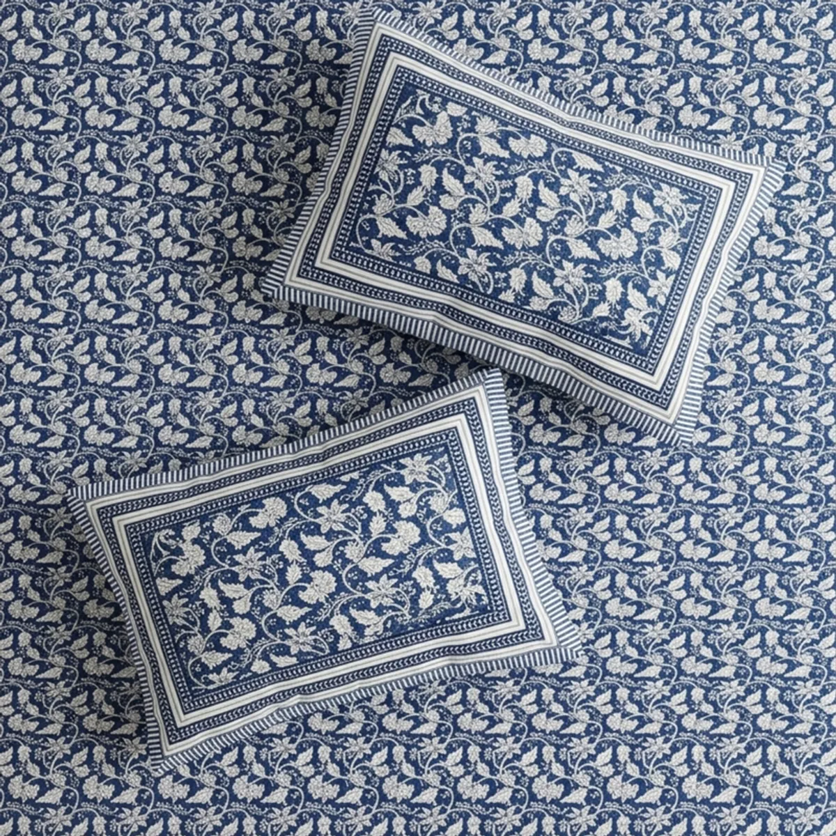 Detailed view of blue floral bedsheet with bordered edge and white throw