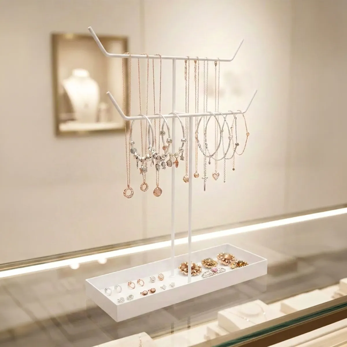 White two-tier jewellery stand displaying necklaces, bracelets and earrings on a counter