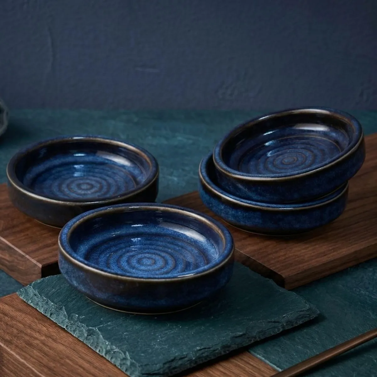 Four blue ceramic dip bowls styled on dark slate and wooden blocks
