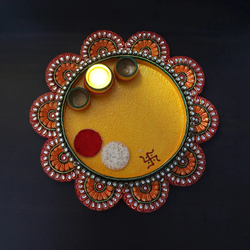 Top view of yellow pooja thali with decorative border, three bowls and ritual items