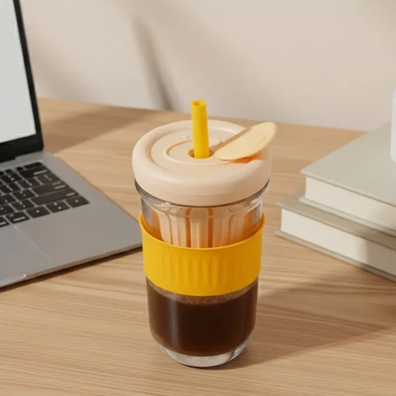 Glass tumbler with orange grip, lid and infuser beside a laptop
