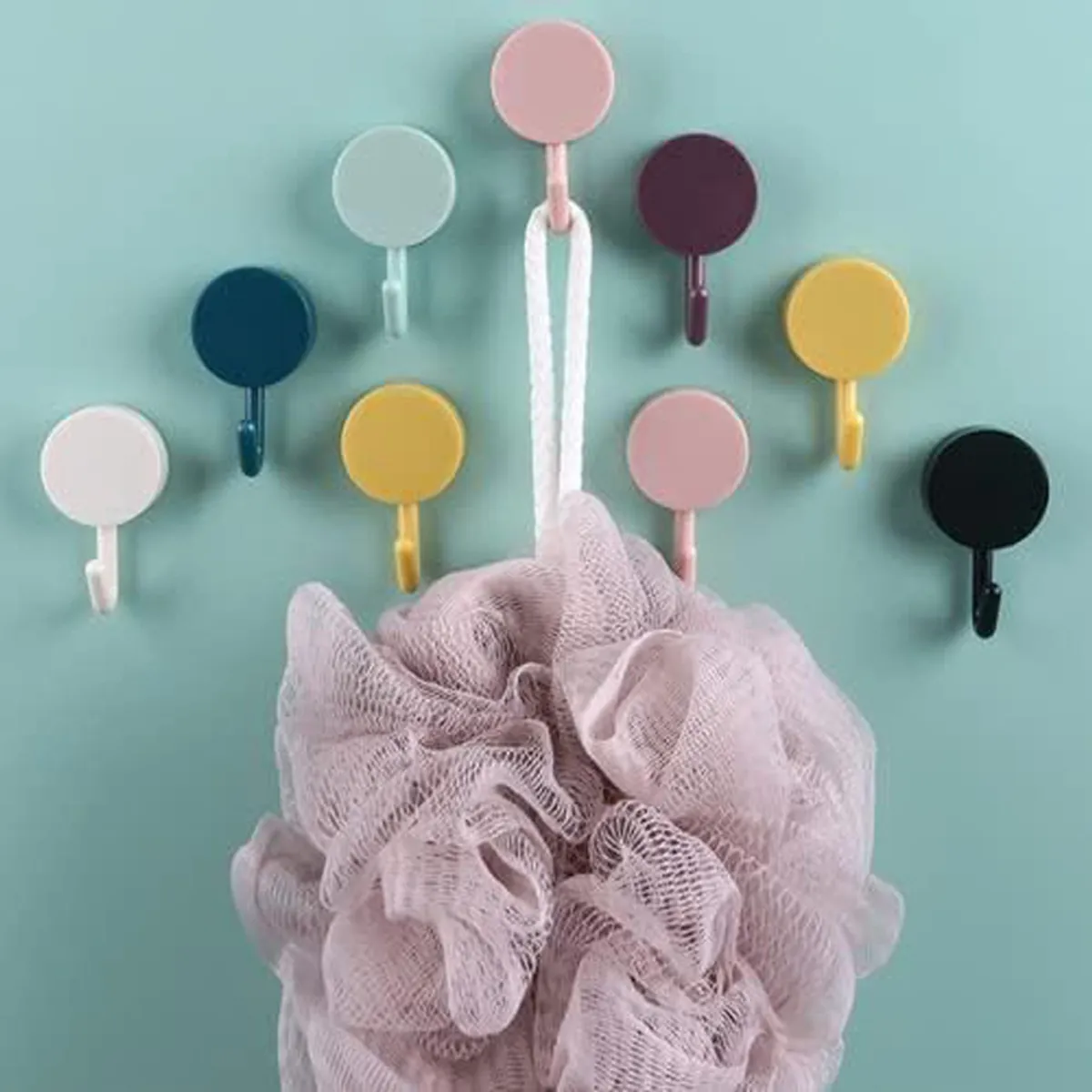 Multicolour round wall hooks arranged on a teal wall, holding a bath sponge.