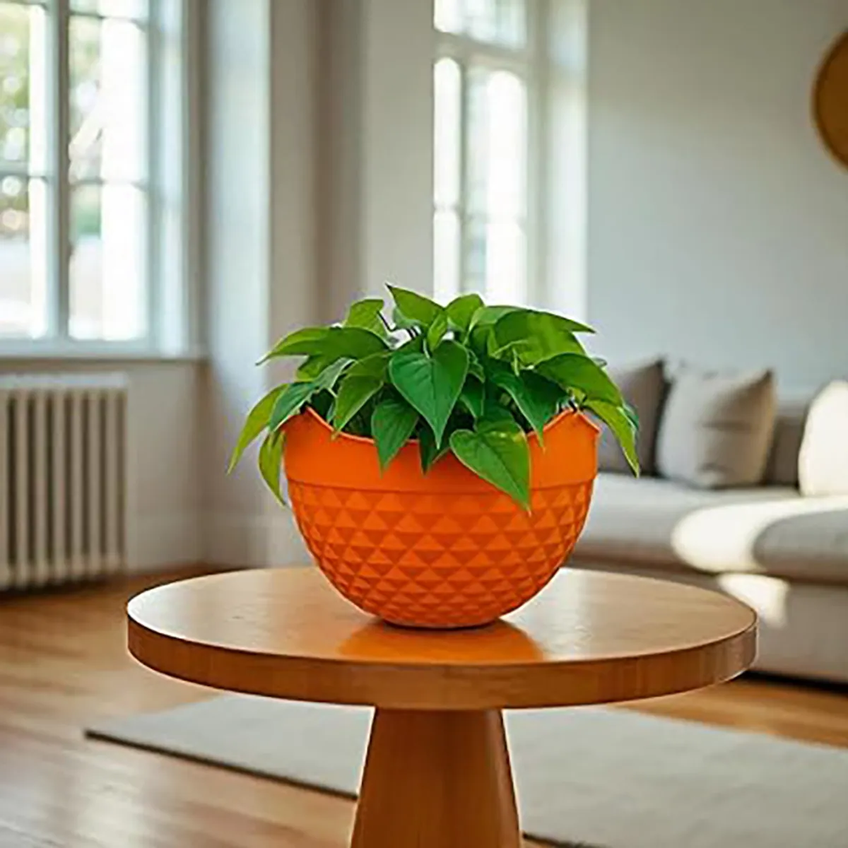 Orange planter with a green plant displayed on a round wooden table.