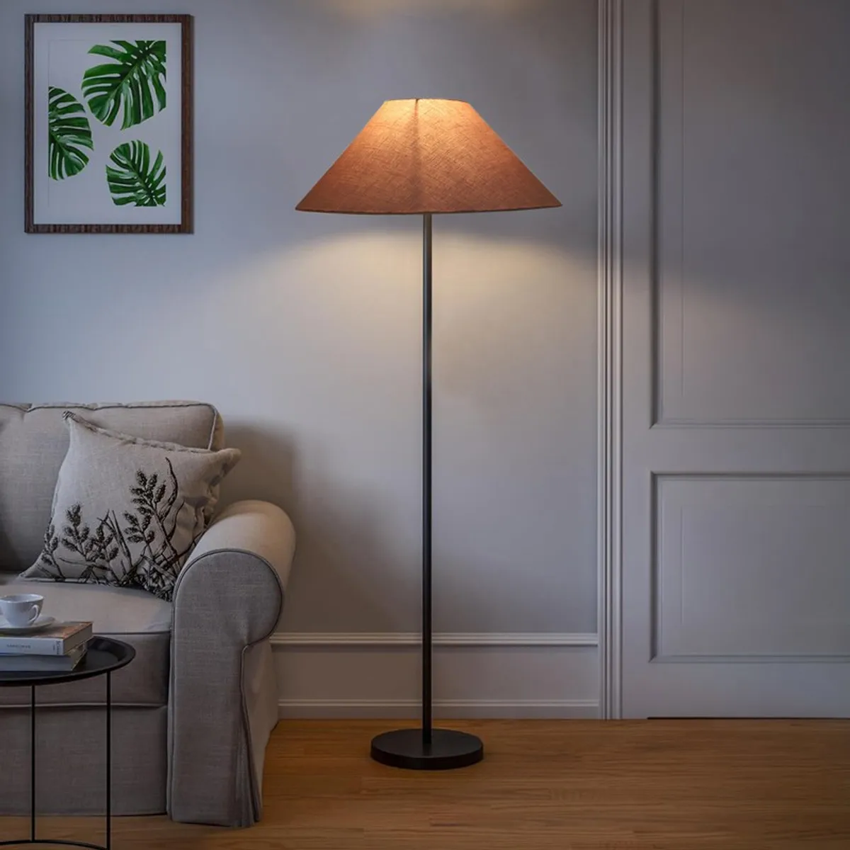 Lit floor lamp with cone shade beside a sofa in a softly lit room