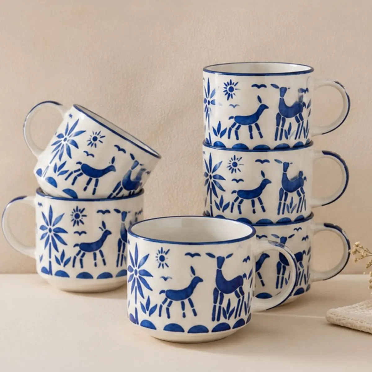 Six white and blue patterned ceramic cups stacked and arranged against a neutral wall.