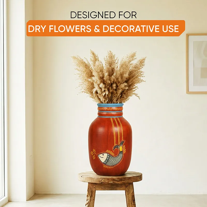 Red terracotta vase with dried stems placed on a rustic wooden stool near a window.
