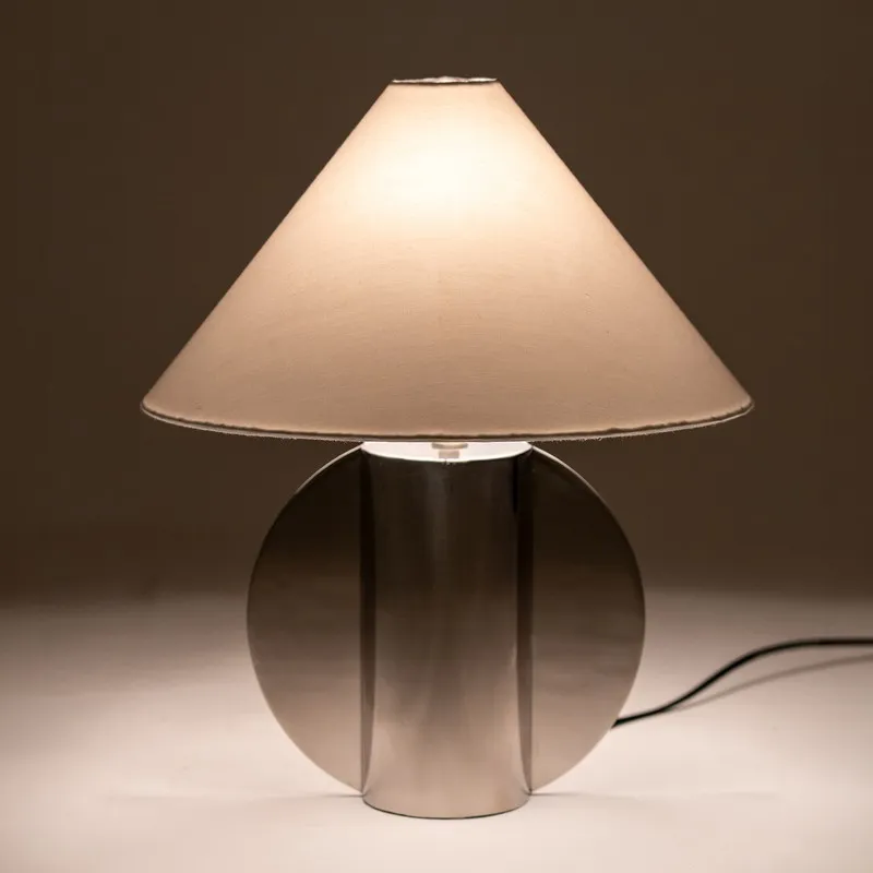 Lit table lamp with white shade and reflective silver base against dark backdrop