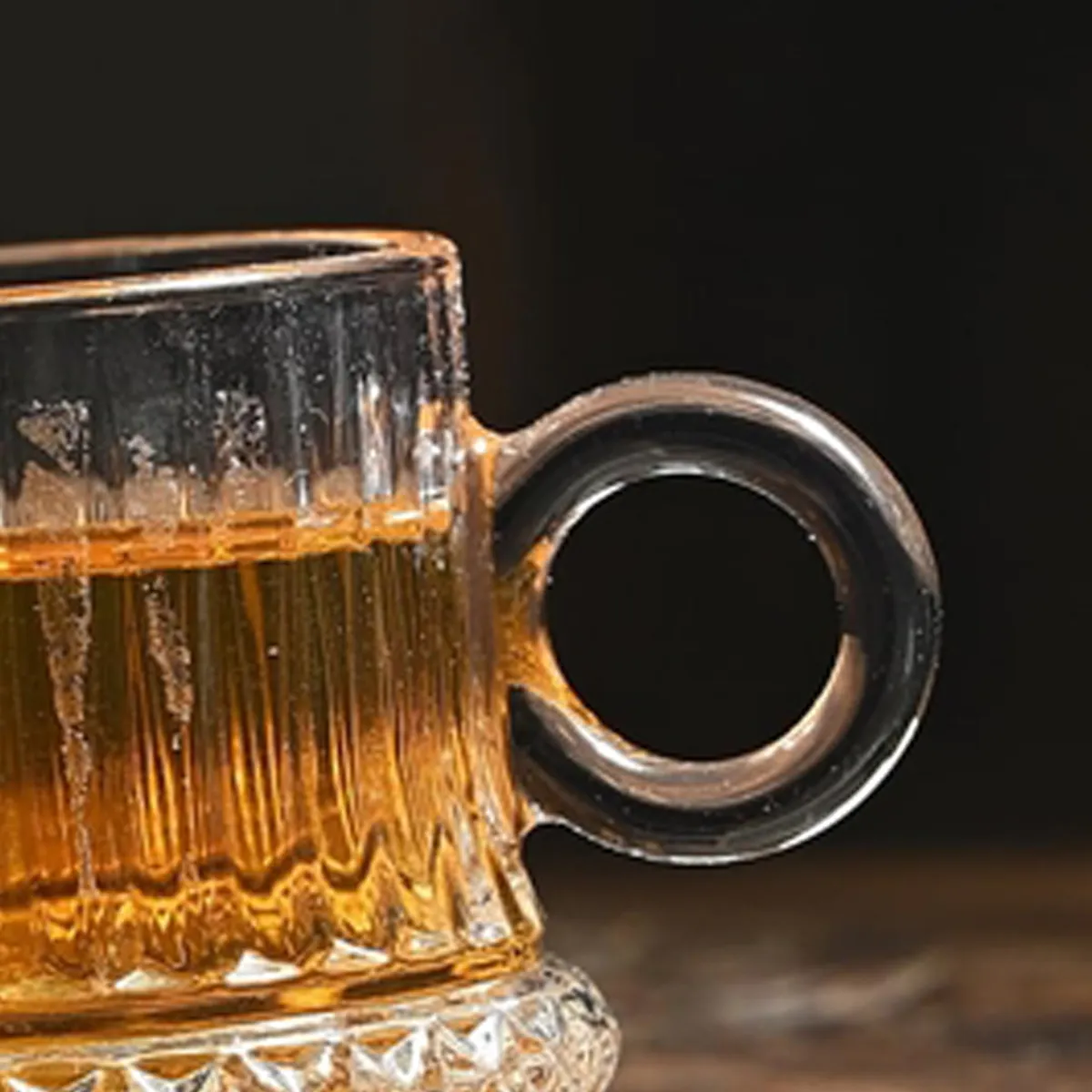 Close-up of the transparent glass cup's round handle and vertical textured sides.