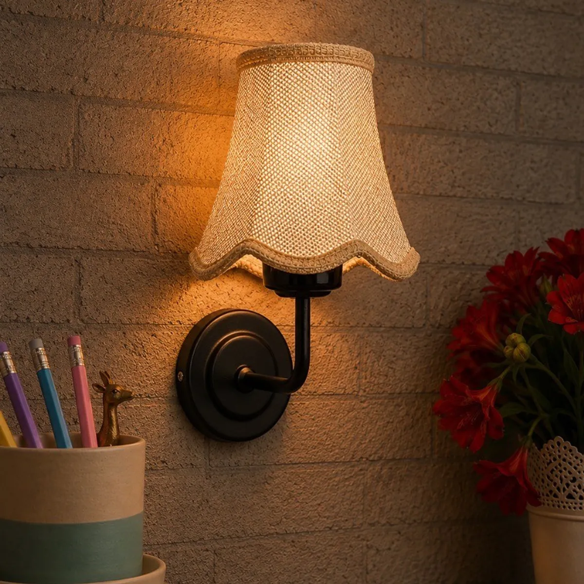 Beige jute wall lamp glowing on a textured wall beside flowers