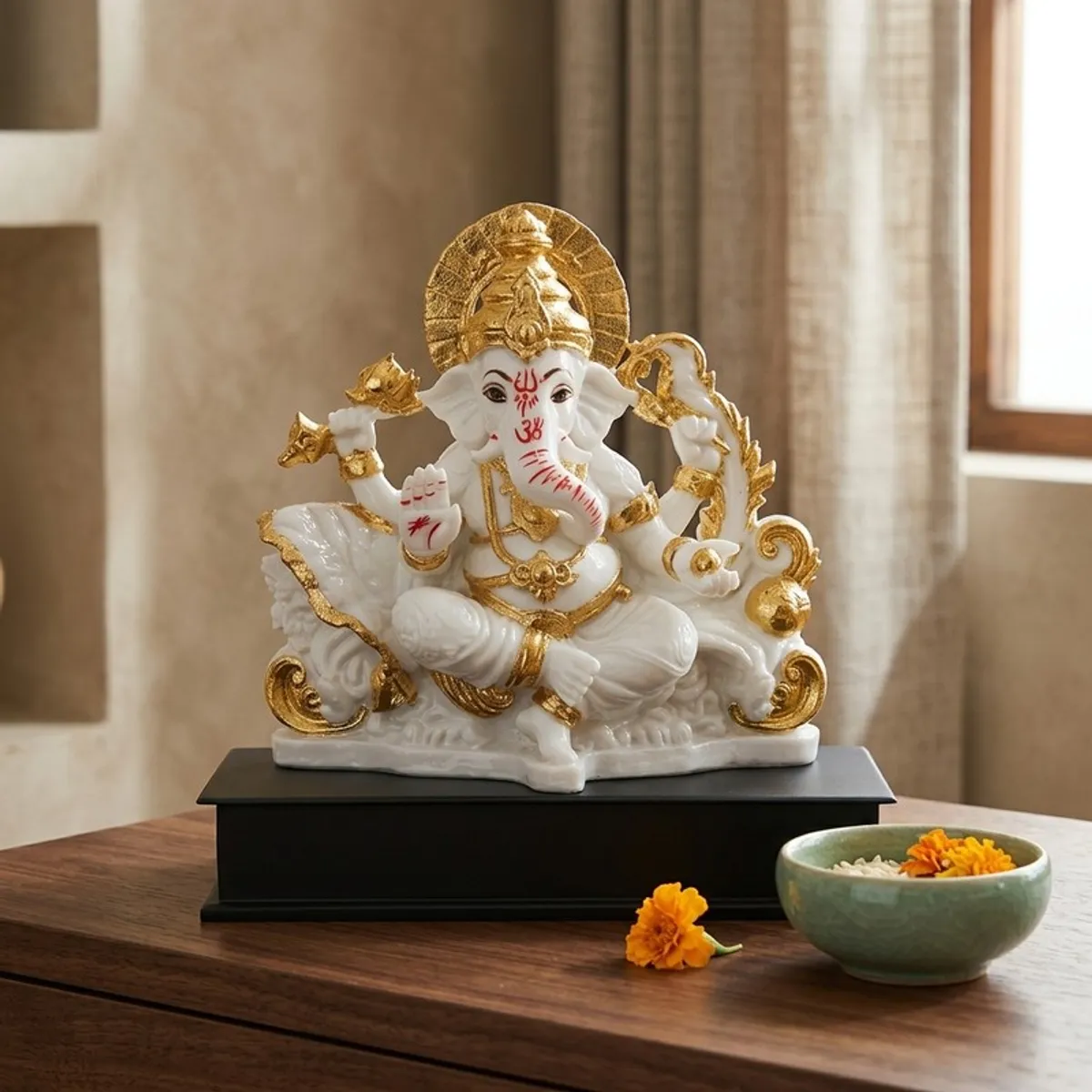White and gold Ganesha idol displayed on a wooden table beside flowers