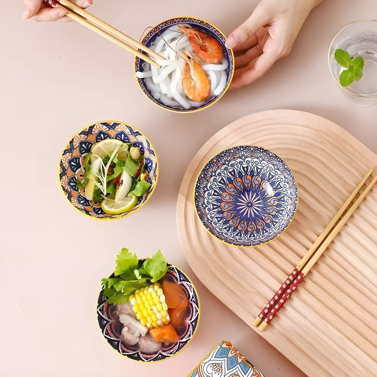 Four colourful patterned bowls arranged with food on a wooden serving board.