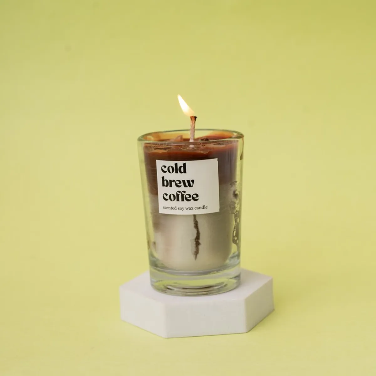 Lit brown coffee candle in a clear glass jar on a white stand