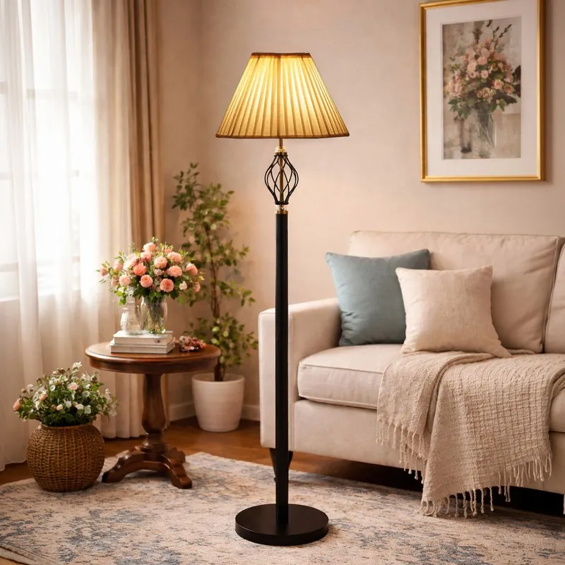 Warm lit floor lamp with pleated shade beside a sofa and round side table