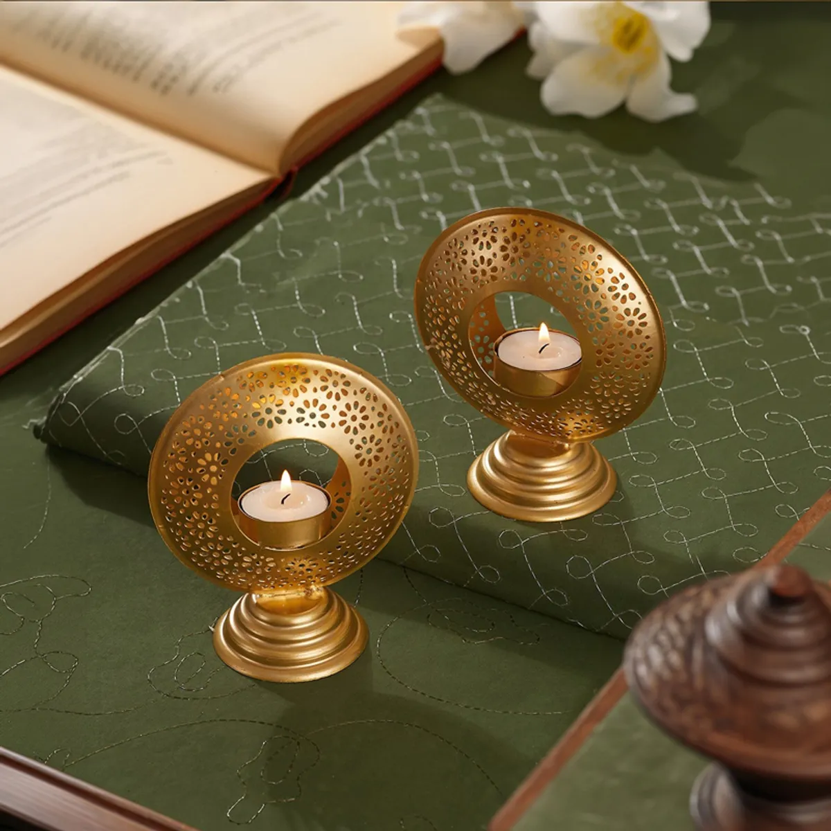 Two gold ornate tealight holders with lit candles on a green surface