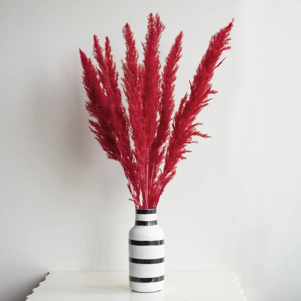 Red dried grass sticks displayed in a striped vase on a tabletop