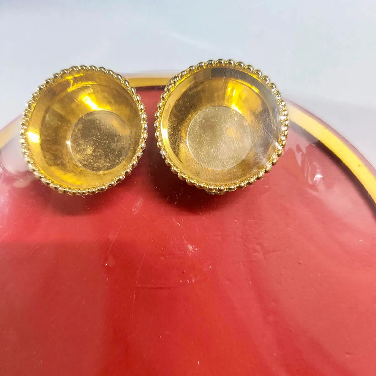 Close-up of two gold-toned bowls placed on the maroon pooja thali