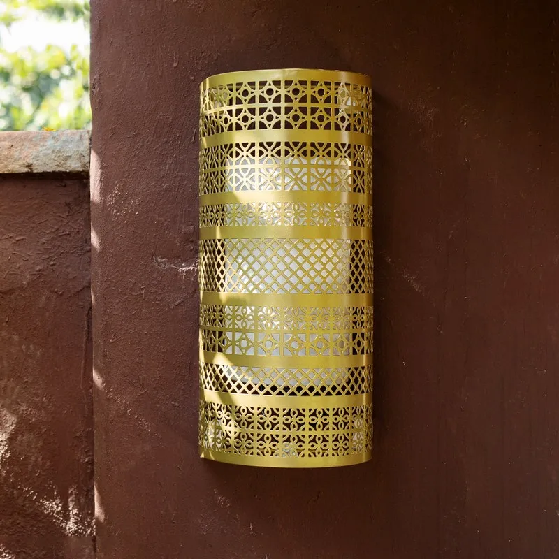 Gold cylindrical lattice wall lamp mounted on a brown textured wall
