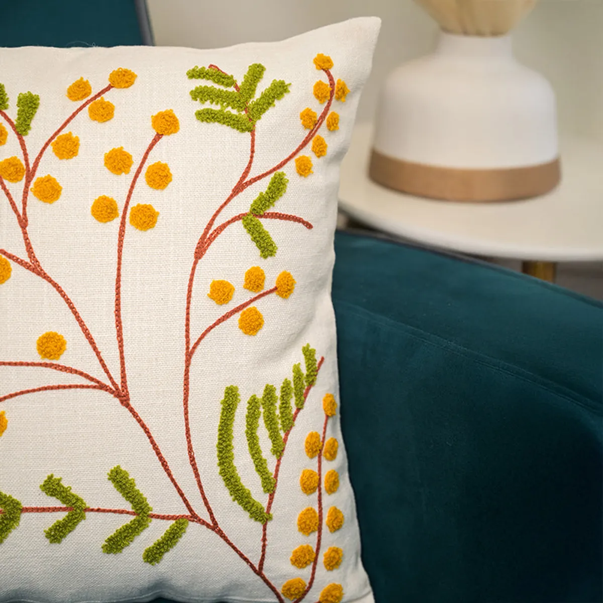 Close-up side view of ivory botanical cushion cover on a teal chair