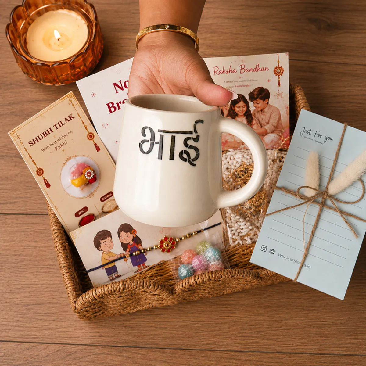 Hand holding the ceramic Bhai mug above a festive Raksha Bandhan hamper