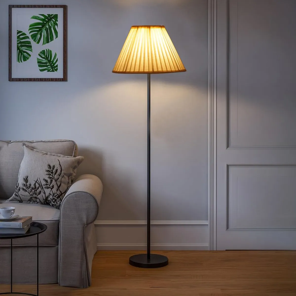 Pleated floor lamp lit in a living room corner beside a beige sofa