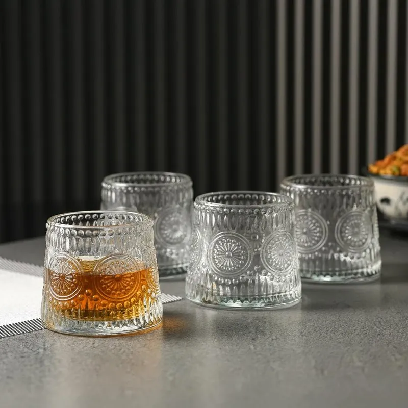 Four clear glass whiskey tumblers, one filled with amber drink