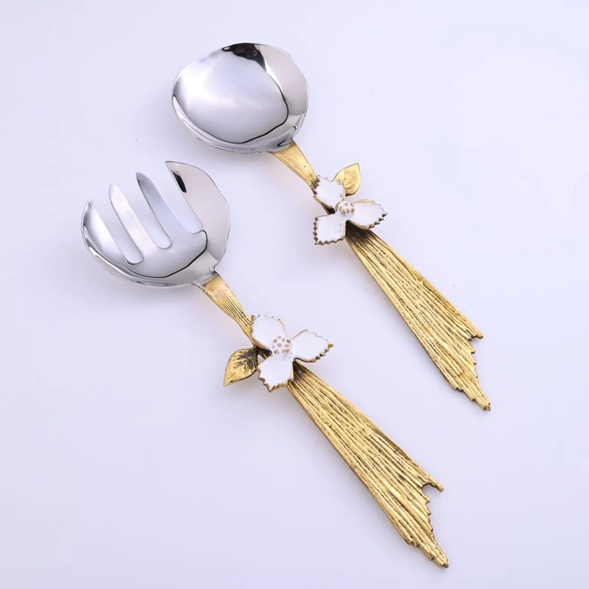 Two silver and gold salad servers with floral details on a light background
