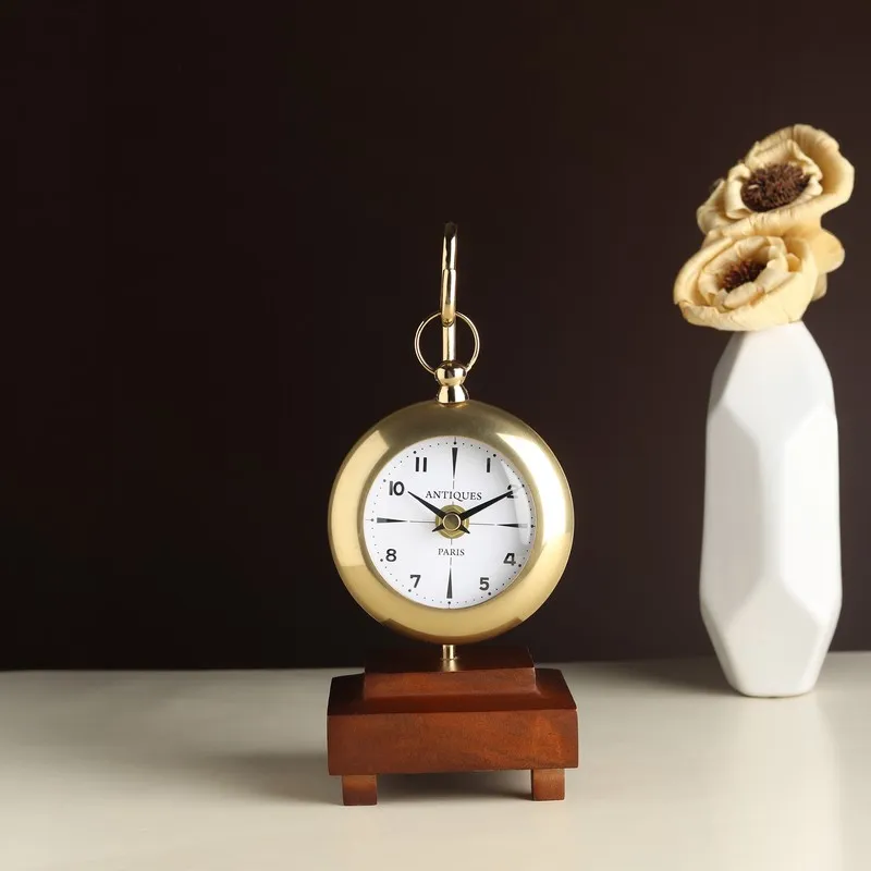 Front view of a gold round table clock on a stepped wooden pedestal base