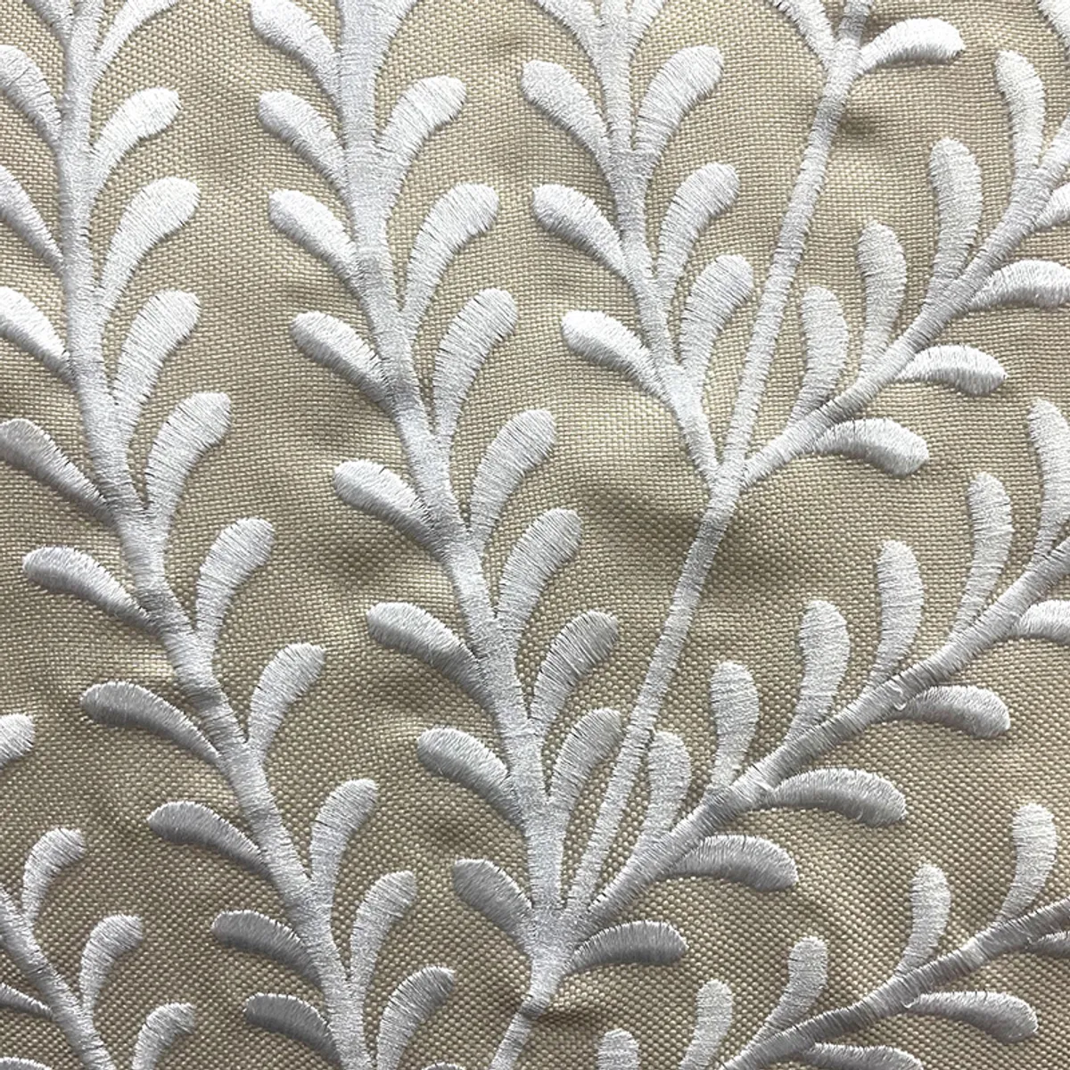 Close-up of white leafy embroidery on a beige cushion cover