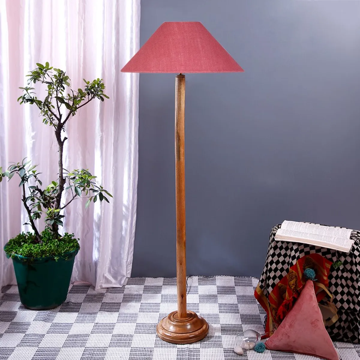 Tall wooden floor lamp with a pink shade beside a potted plant and draped table