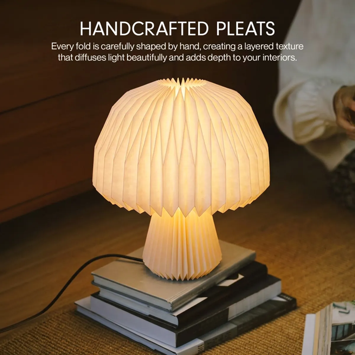 Pleated mushroom lamp glowing on stacked books beside a bed