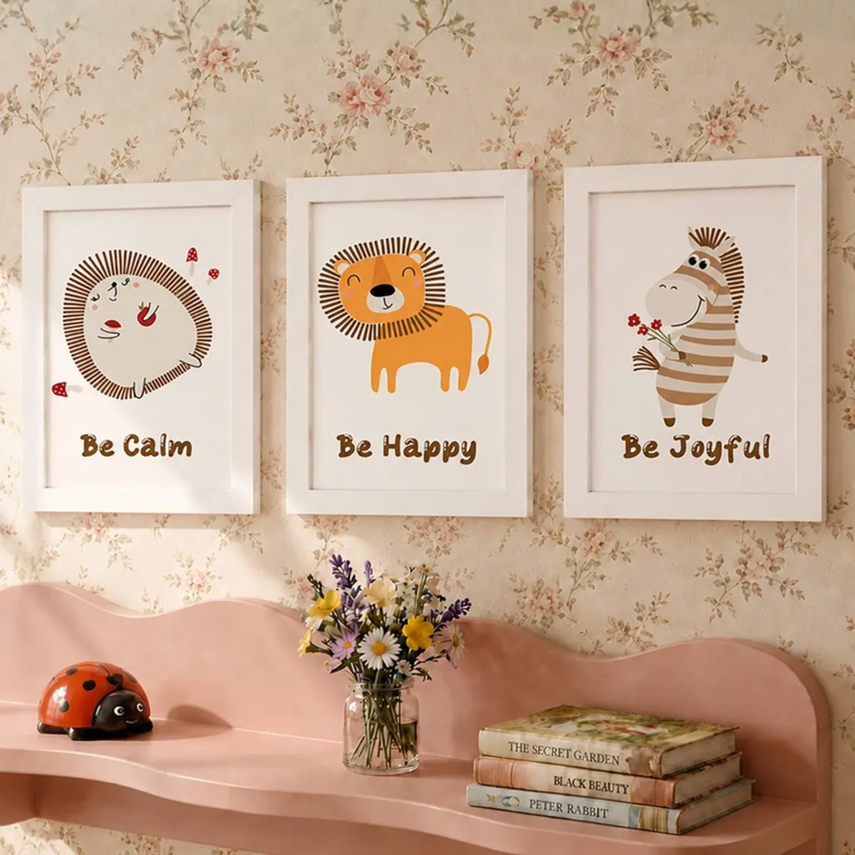 Three white-framed safari animal prints on a floral wall above a pink shelf