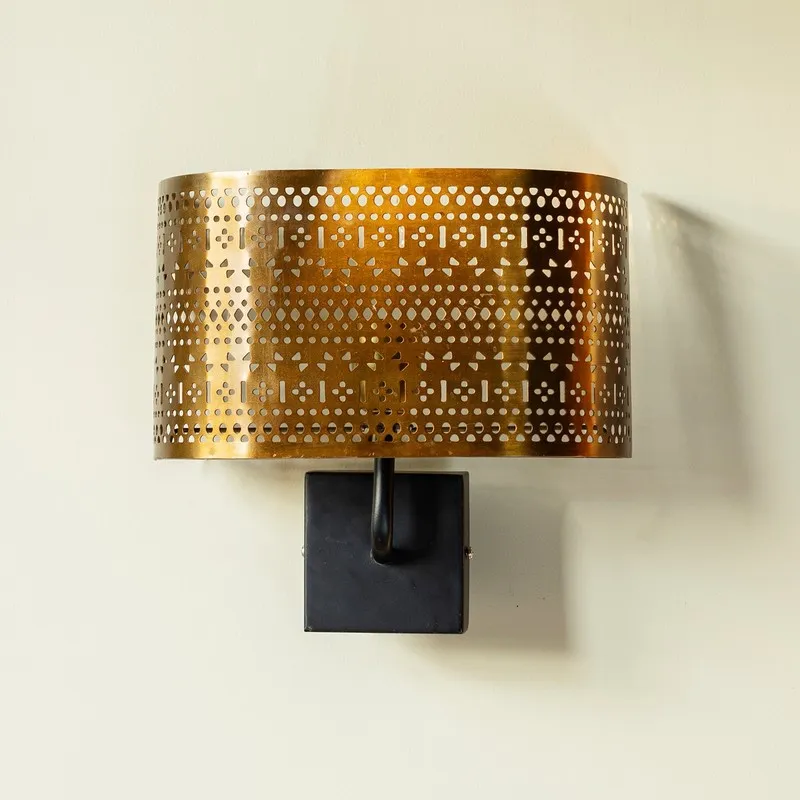 Gold cylindrical wall lamp with black wall mount against a light wall