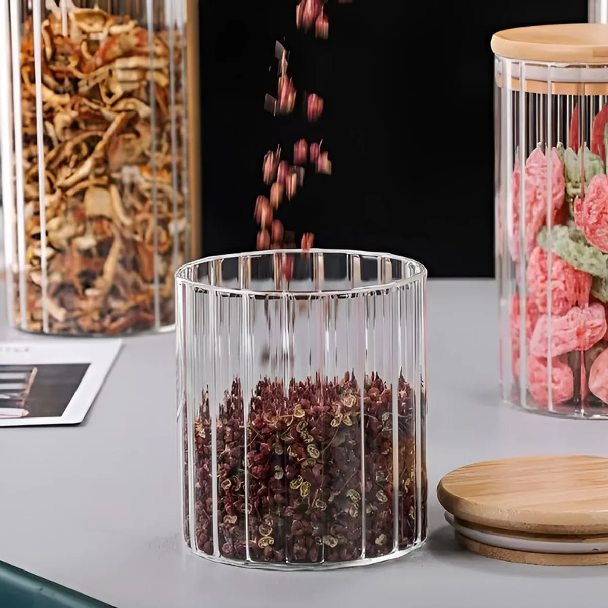 Open fluted glass jar beside its bamboo lid, shown with spices and snacks.