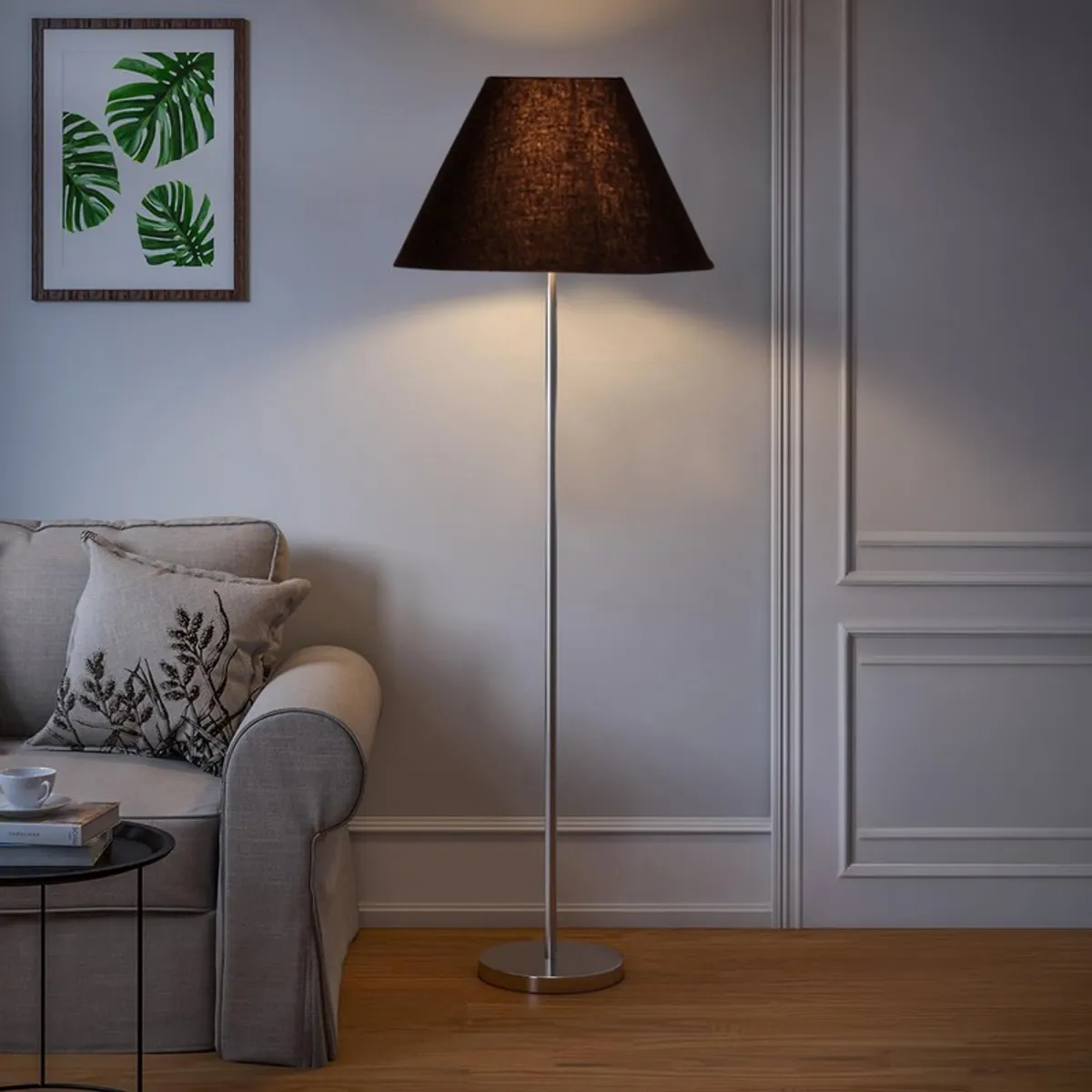Black floor lamp glowing beside a sofa in a neutral living room
