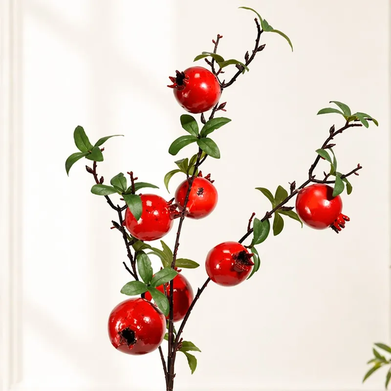 Close-up of artificial pomegranate branch with glossy red fruit and green leaves