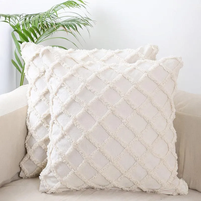 Two white tufted cushion covers layered on a white armchair with a palm leaf behind.