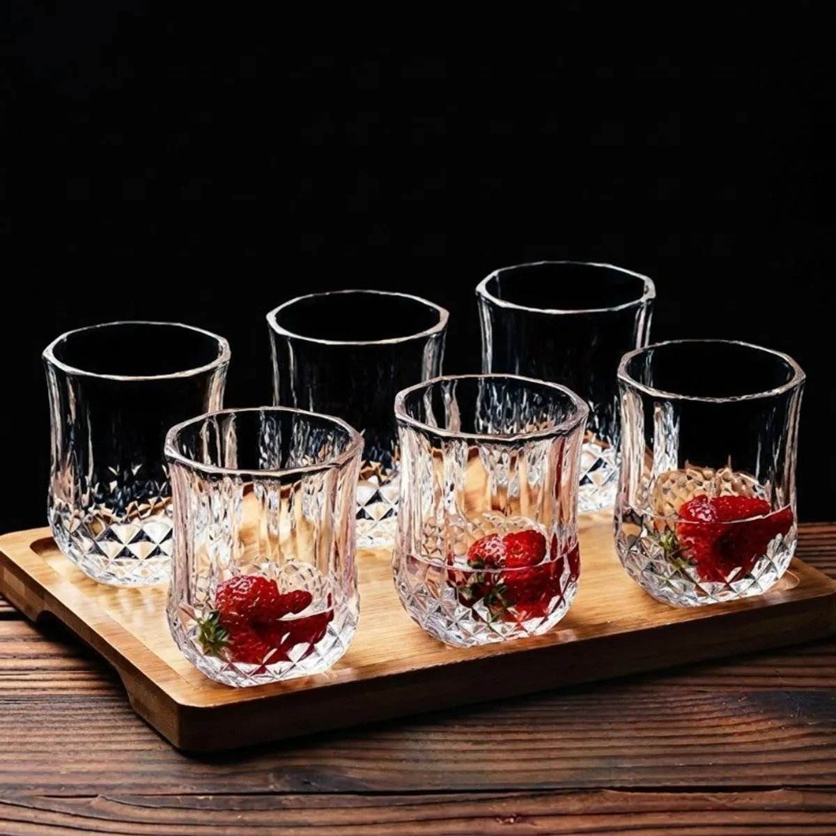 Six clear textured glasses with strawberries on a wooden serving board